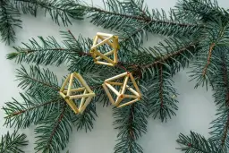 Trzy ozdoby choinkowe ze słomy w kształcie brył geometrycznych wiszą na gałęzi świerku.