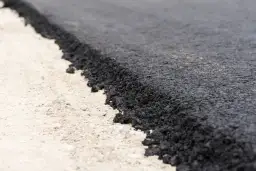 Zbliżenie na świeżo położony asfalt na jasnym podłożu.