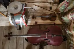 Instrument ludowy podobny do wiolonczeli, skrzypce i bębenek leżą na drewnianej podłodze.
