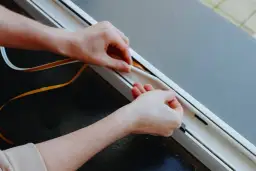 Dłonie przyklejają uszczelkę do ramy drzwi wewnętrznych. Prosty sposób, jak zamontować uszczelki w drzwiach wewnętrznych.