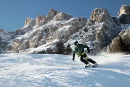 Narciarz szusuje po ośnieżonym stoku, w tle majestatyczne góry Alpy.