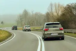 Samochody na mglistej drodze. Myśląc o tym, jak wyrobić prawo jazdy, warto pamiętać o ostrożności na zakrętach.