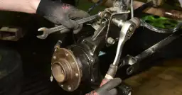 Mechanik w rękawiczkach dokonuje wymiany łożyska koła, używając kluczy do odkręcenia elementów zawieszenia.