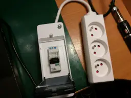 Wyłącznik nadprądowy Eaton w obudowie obok białego przedłużacza z trzema gniazdami.