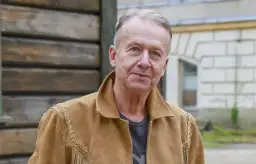 Bogusław Linda w brązowej kurtce z zamszu, z frędzlami i ozdobnymi szwami.