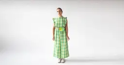 Kobieta w zielonym kombinezonie w kratkę, z kolorową nerką na biodrach, na białym tle.