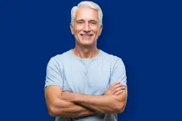 Uśmiechnięty starszy mężczyzna z siwymi włosami i wąsami, w jasnoniebieskiej koszulce, z rękami skrzyżowanymi na piersi. Wygląda jak żywy dowód na to, że wiek to tylko liczba, efekt Galatei w czystej postaci.