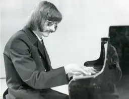 Mieczysław Kosz w okularach i garniturze gra na fortepianie.