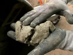 Rękawice robocze trzymają grudki zaschniętego betonu, co jest pierwszym krokiem w procesie, jak wyczyścić betoniarkę.