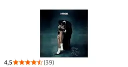 Rihanna w czarnym garniturze, siedząca z głową opuszczoną na dłonie, na tle mrocznego gradientu.
