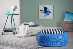 Niebieskie i białe pufy z opon do ogrodu, ozdobione poduszkami w marynistyczne wzory, tworzą przytulny kącik.