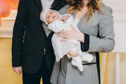 Rodzice trzymają niemowlę w białym ubranku, idealnym na chrzest zimą.