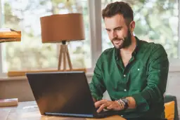 Mężczyzna w zielonej koszuli pracuje przy laptopie, tworząc **lead artykułu** o pracy zdalnej.