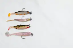 Cztery gumowe przynęty wędkarskie w kształcie rybek, ułożone jedna pod drugą na białym tle.