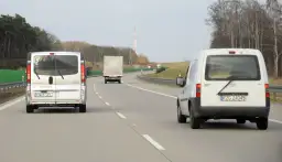 Na autostradzie widać kilka pojazdów, w tym dwa białe busy i jeden tir. Zastanawiasz się, ile tir może jechać na autostradzie?