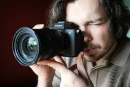 Mężczyzna zamyka oko, patrząc przez wizjer aparatu Sony Alpha 7. Premiera Sony a7 IV budzi emocje.