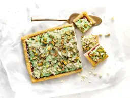 Ciasto z zieloną masą pistacjową i posiekanymi pistacjami, pokrojone na kwadraty.