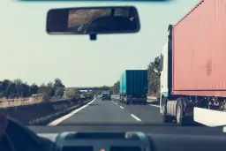Widok z kabiny samochodu na autostradzie z ciężarówkami i innymi pojazdami.