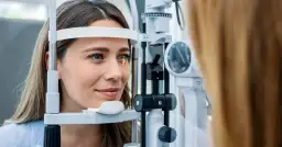 Kobieta podczas badania wzroku w gabinecie okulistycznym, z użyciem sprzętu optycznego.