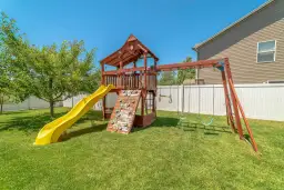 Drewniany plac zabaw z żółtą zjeżdżalnią, ścianką wspinaczkową i huśtawkami na zielonym trawniku.