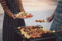 Ludzie grillują szaszłyki z mięsem i warzywami na grillu.