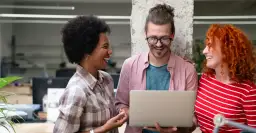 Drei lachende Personen mit Laptop im Büro.