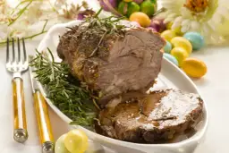 Pyszne pieczone mięso z rozmarynem, idealne jako co na obiad na Wielkanoc. Kolorowe jajka i kwiaty dodają świątecznego klimatu.