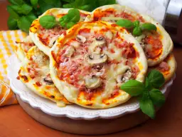 Szybkie mini pizze z szynką i pieczarkami, ozdobione świeżą bazylią, kuszą apetycznym wyglądem.