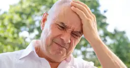 Mężczyzna z ręką na czole, cierpiący z powodu ataków złości, które mogą być objawem choroby.