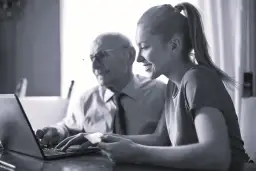 Starszy mężczyzna i młoda kobieta patrzą na laptopa, kobieta trzyma kartę.