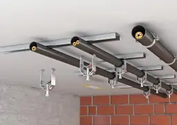 Systemy tras kablowych zamontowane pod sufitem, zgodne z zasadami prowadzenia tras kablowych. Metalowe uchwyty mocują czarne rury z kablami.