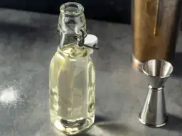 Domowy syrop cukrowy (simple syrup) w butelce, obok jigger i shakera. Idealny do drinków, łatwy do przygotowania krok po kroku.