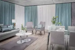 Eleganckie firany w salonie tworzą przytulną atmosferę. Szare fotele i kanapa dopełniają nowoczesny wystrój.