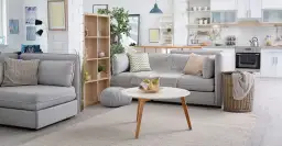 Nowoczesny salon z aneksem kuchennym. Miękka sofa, stolik kawowy z owocami i kosz na pranie. To wszystko warto objąć ubezpieczeniem mienia.