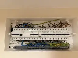 Widok otwartej skrzynki z bezpiecznikami i przewodami elektrycznymi.