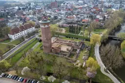Ruiny zamku krzyżackiego w Brodnicy z charakterystyczną wieżą, otoczone zielenią i wodą, w tle rozciąga się miasto.