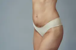 Bok kobiety z widocznym pępkiem i linią bioder w jasnej bieliźnie.