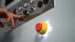 Ręka naciska przycisk na panelu sterowania. Obok świeci przycisk bezpieczeństwa, ilustrujący styk bezpotencjałowy schemat.