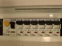 Panel z bezpiecznikami Eaton, z etykietami opisującymi obwody: lodówka, pokój D, zmywarka, łazienka, oświetlenie.