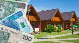 Polskie banknoty na tle drewnianych domków letniskowych.