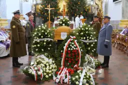 Trumna w otoczeniu wieńców, żołnierze w mundurach stoją na straży.