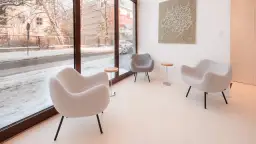 Nowoczesna fotografia wnętrz: trzy szare fotele i stoliki tworzą przytulną poczekalnię z widokiem na zimowy krajobraz.