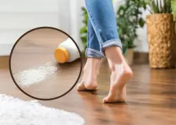 Zbliżenie na butelkę z talkiem i rozsypany proszek na drewnianej podłodze, obok bosej stopy.