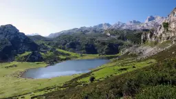 Lago en un valle montañoso verde con picos rocosos al fondo.
