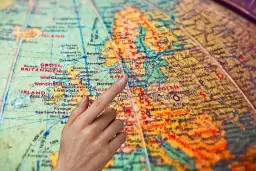 Dłoń wskazująca palcem na mapę Europy, z zaznaczonymi Wielką Brytanią i Polską.