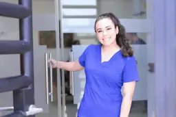 Uśmiechnięta pielęgniarka w niebieskim uniformie otwiera drzwi. Czy zastanawiasz się, ile zarabia pielęgniarka pediatryczna?