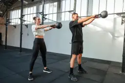 Kobieta i mężczyzna wykonują ćwiczenia z kettlebellami w siłowni.