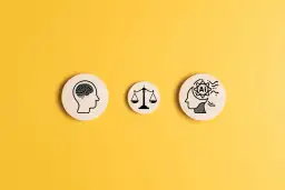 Trzy drewniane krążki na żółtym tle: ludzki mózg, waga sprawiedliwości i głowa z symbolem AI w środku, ilustrują, jak sztuczna inteligencja może rozwiązać dylematy etyczne.