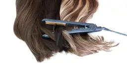 Prostownica do włosów w trakcie kręcenia pasm ciemnych i blond.