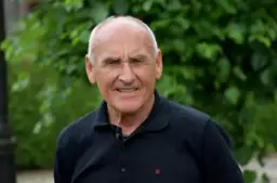 Starszy mężczyzna w czarnej koszulce polo, z siwymi włosami i zmarszczkami na twarzy, uśmiecha się. Co się stało Langowi?